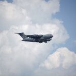A US Air Force C-17 Globemaster III aircraft flying amidst fluffy clouds in a clear blue sky.